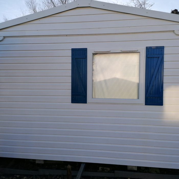 Façade de mobil-home avec bardage propre et volets bleus après nettoyage